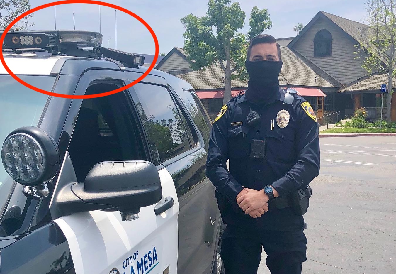 A masked police officer stands next to a patrol vehicle with two ALPR cameras.